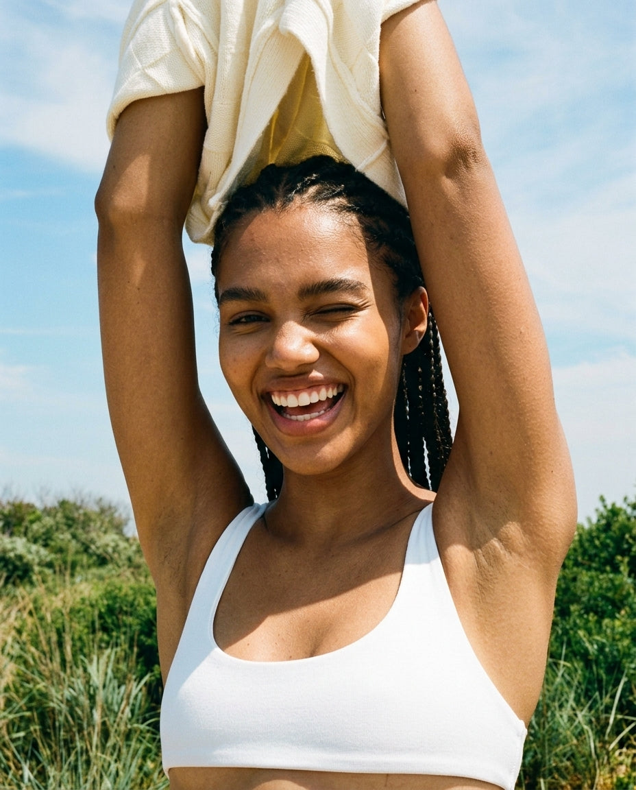 Smiling person pulling a shirt over their head outdoors